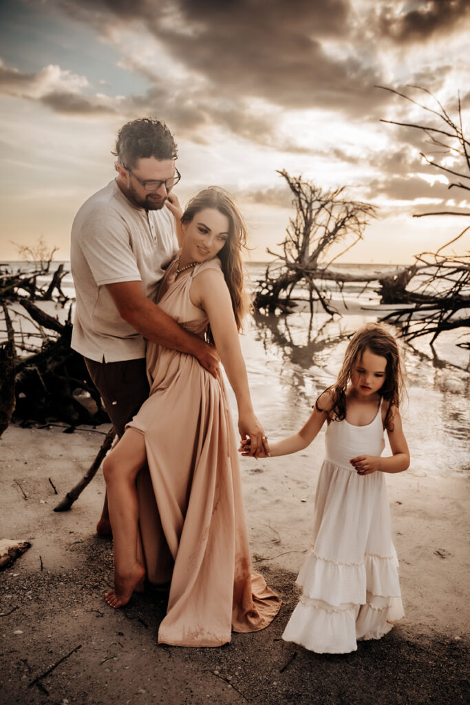 Family Photographer, a husband and wife embrace with their young daughter with them at the beach