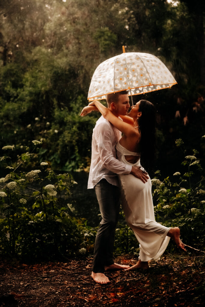 Family Photographer, a man and woman embrace underneath an umbrella in the rain outdoor in nature